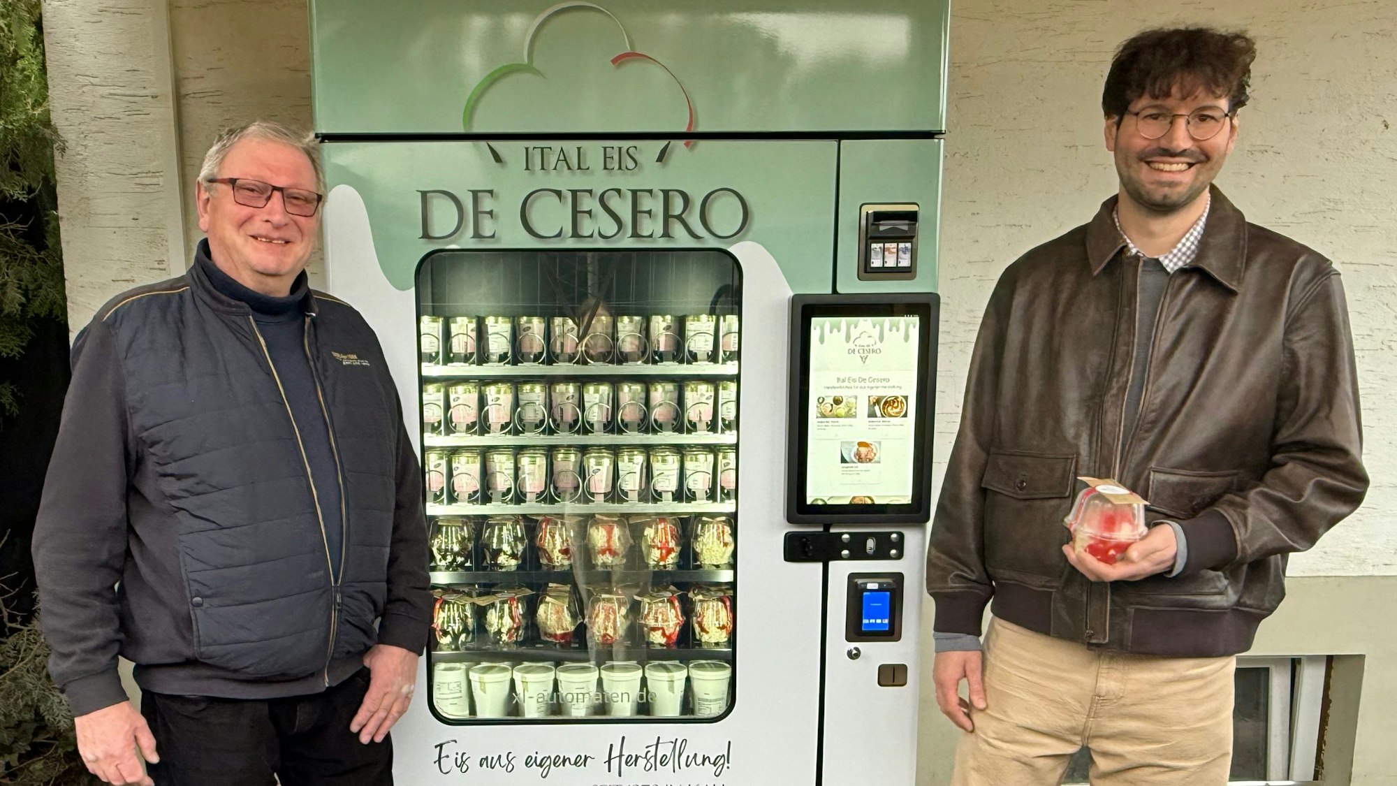 Danilo und Manuel De Cesero stehen an beiden Seiten neben dem gefüllten Eisautomaten.