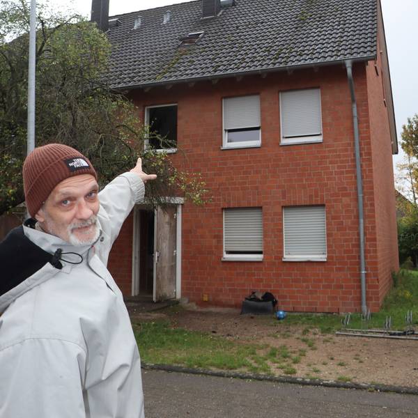 Zu sehen ist, wie ein Mann auf ein Haus deutet.