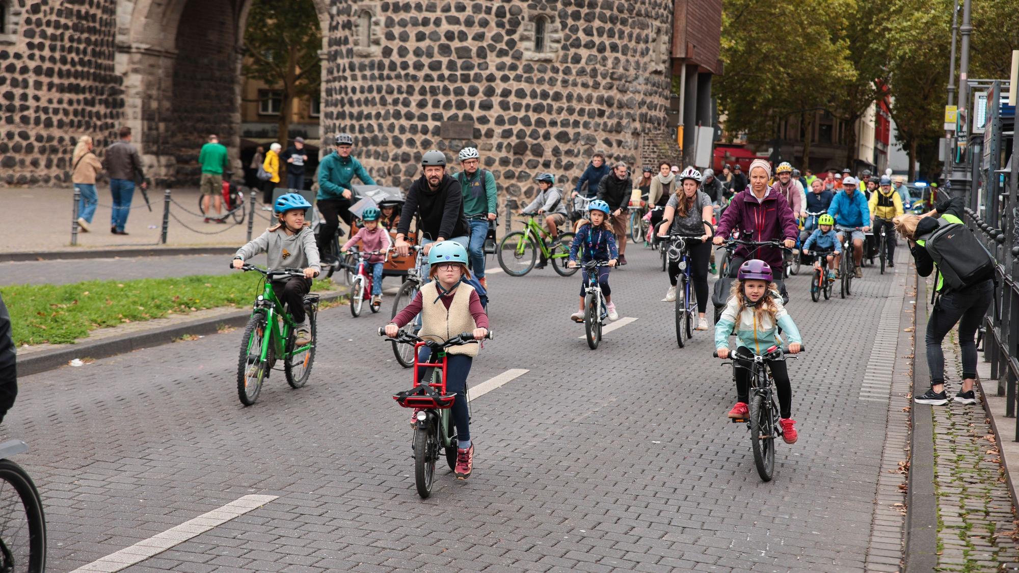 Kinder und Erwachsene auf Fahrrädern befahren die Straße am Rudolfplatz in Köln.