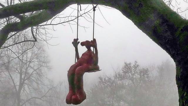 An einem Ast eines mächtigen Baumes baumelt eine Schaukel, darauf sitzt die Skulptur eines Mädchens.