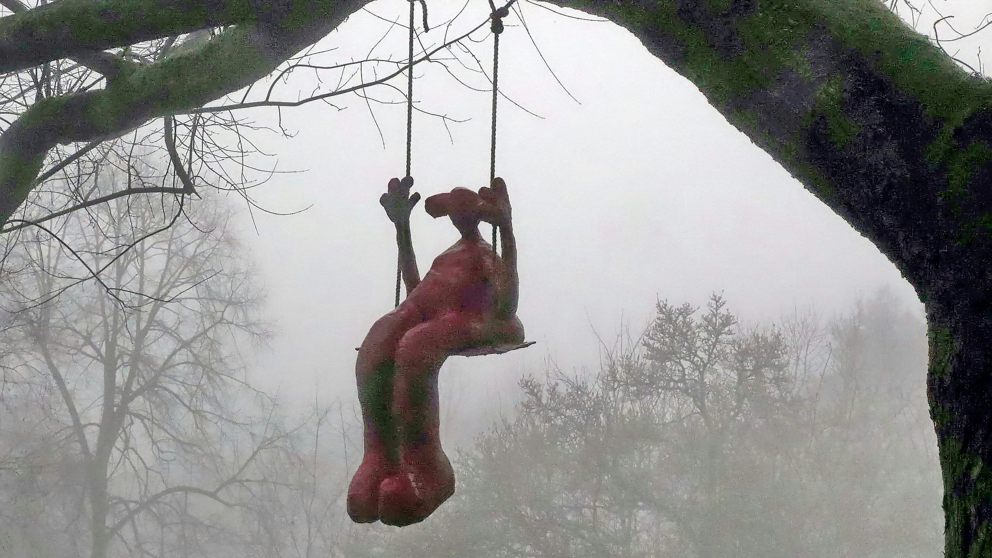 An einem Ast eines mächtigen Baumes baumelt eine Schaukel, darauf sitzt die Skulptur eines Mädchens.