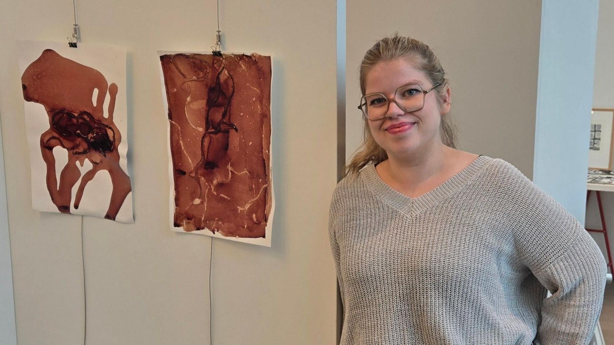 Eine junge Frau neben zwei abstrakten Bildern.