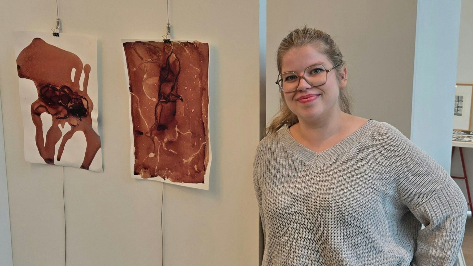 Eine junge Frau neben zwei abstrakten Bildern.