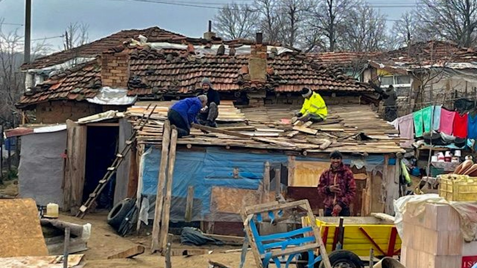 Viel Männer dichten Lücken an einem undichten Dacht einer Baracke mit Holz notdürftig ab.