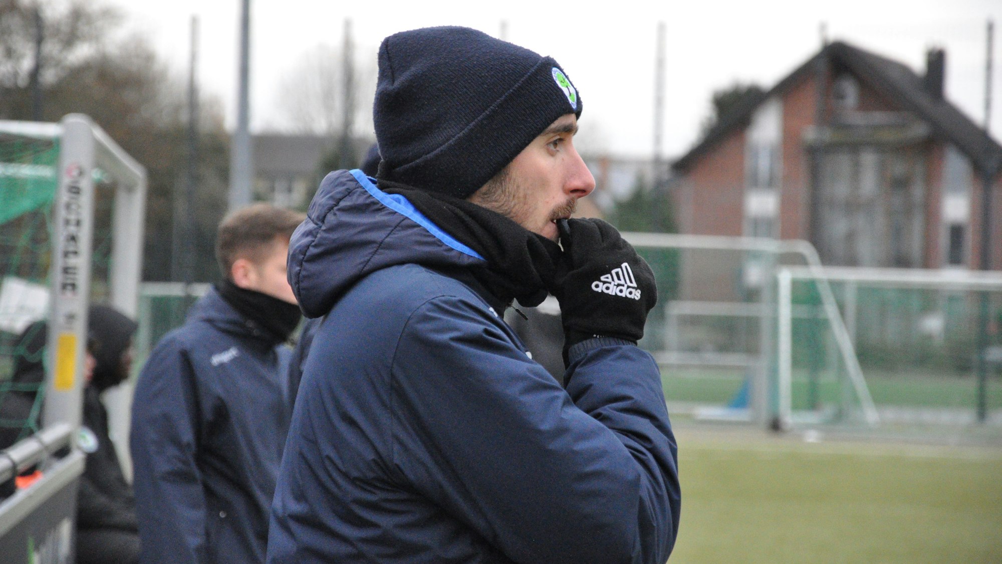 Auf dem Bild ist ein Trainer am Rand eines Fußballfeldes zu sehen.