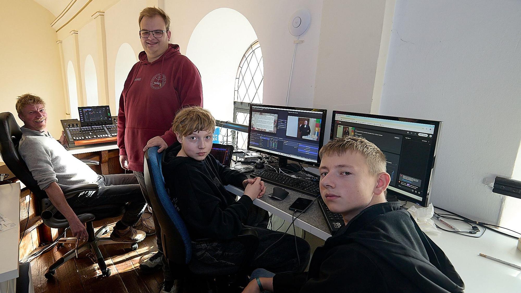 Zwei Männer und zwei Jugendliche sitzen im Hellenthaler Kirchengebäude vor mehreren Computer-Bildschirmen.