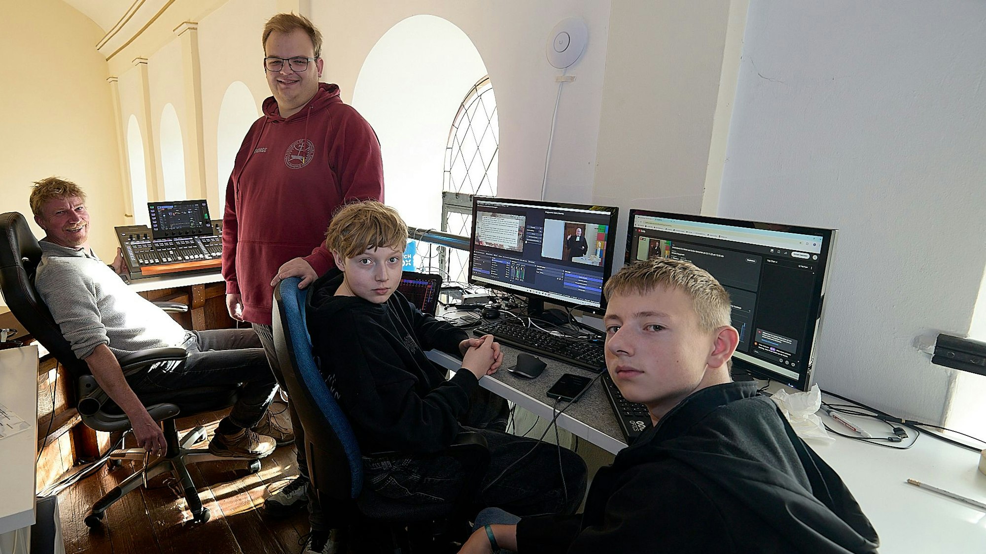 Zwei Männer und zwei Jugendliche sitzen im Hellenthaler Kirchengebäude vor mehreren Computer-Bildschirmen.