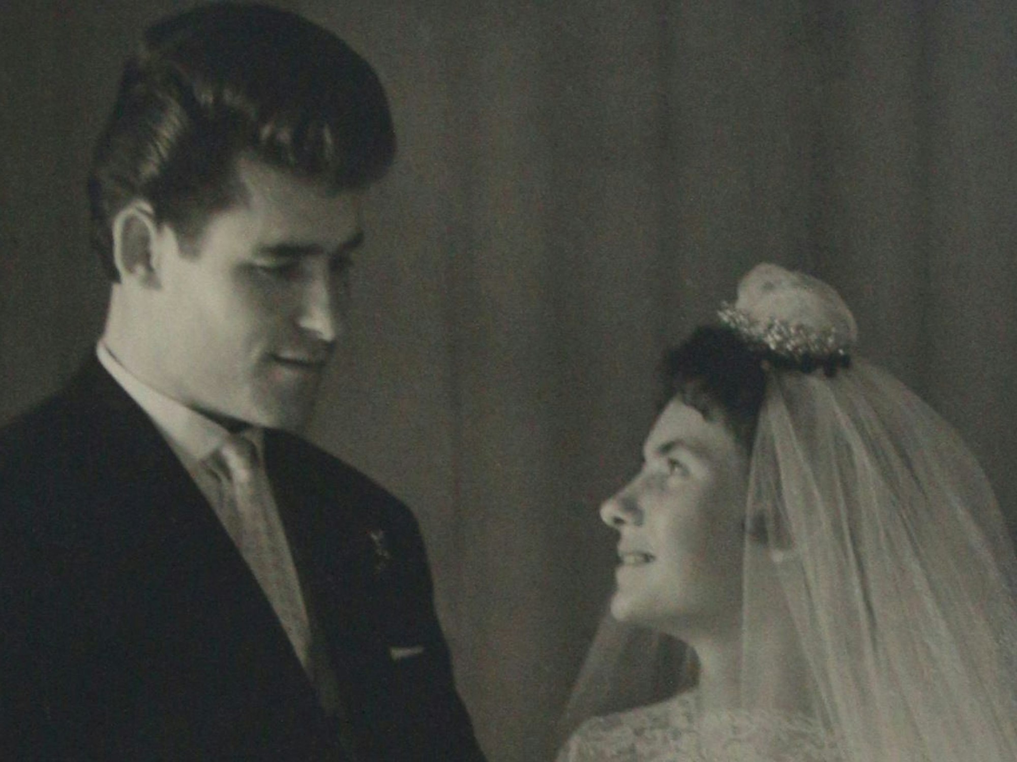 Die Braut im weißen Kleid trägt einen Schleier und ein Krönchen, der Bräutigam lächelt sie an.