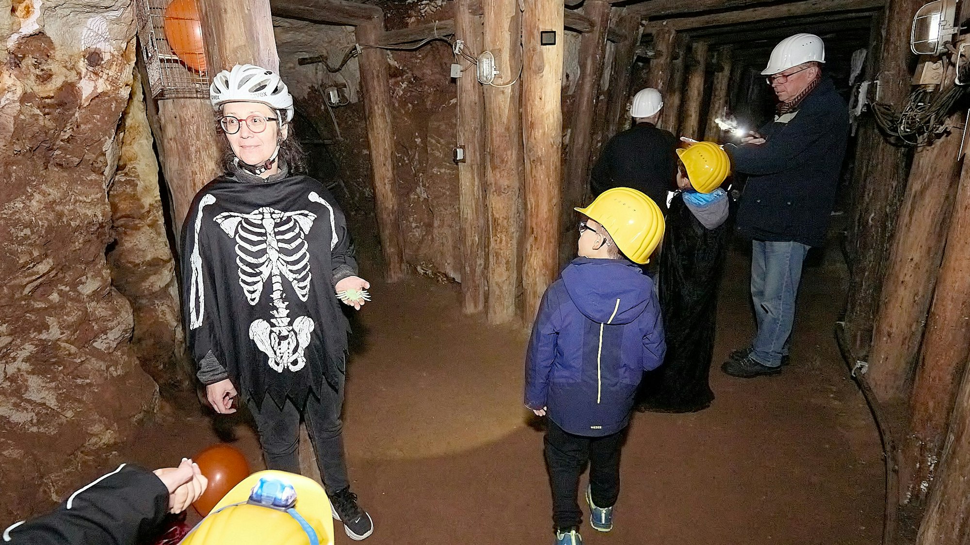 Petra Trimborn steht mit Besuchern in einem Bergwerksstollen. Sie trägt einen Knochen-Overall.