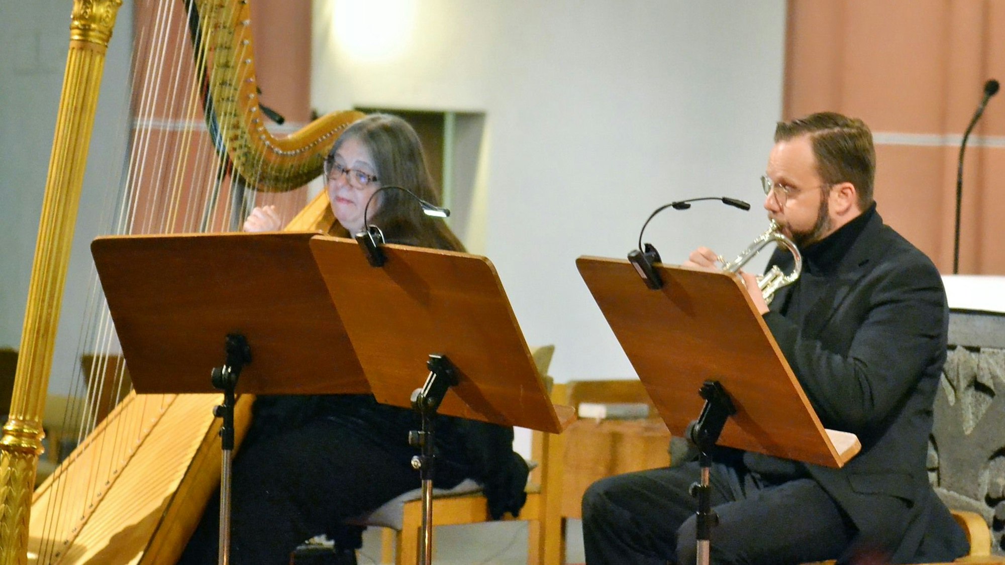Eine Harfenistin und ein Trompeter spielen auf ihre Notenblätter schauend.