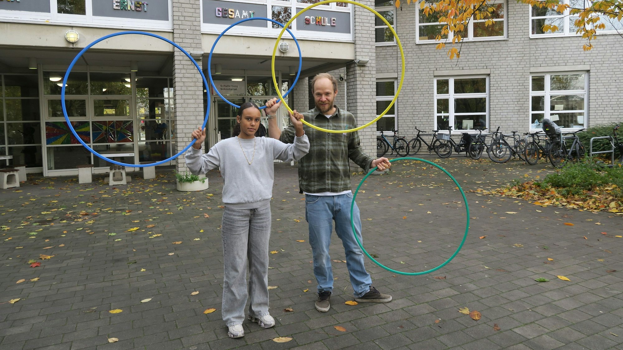 Ein Mädchen steht neben einem Mann im karierten Hemd. Sie halten unterschiedlich große Ringe in die Luft.