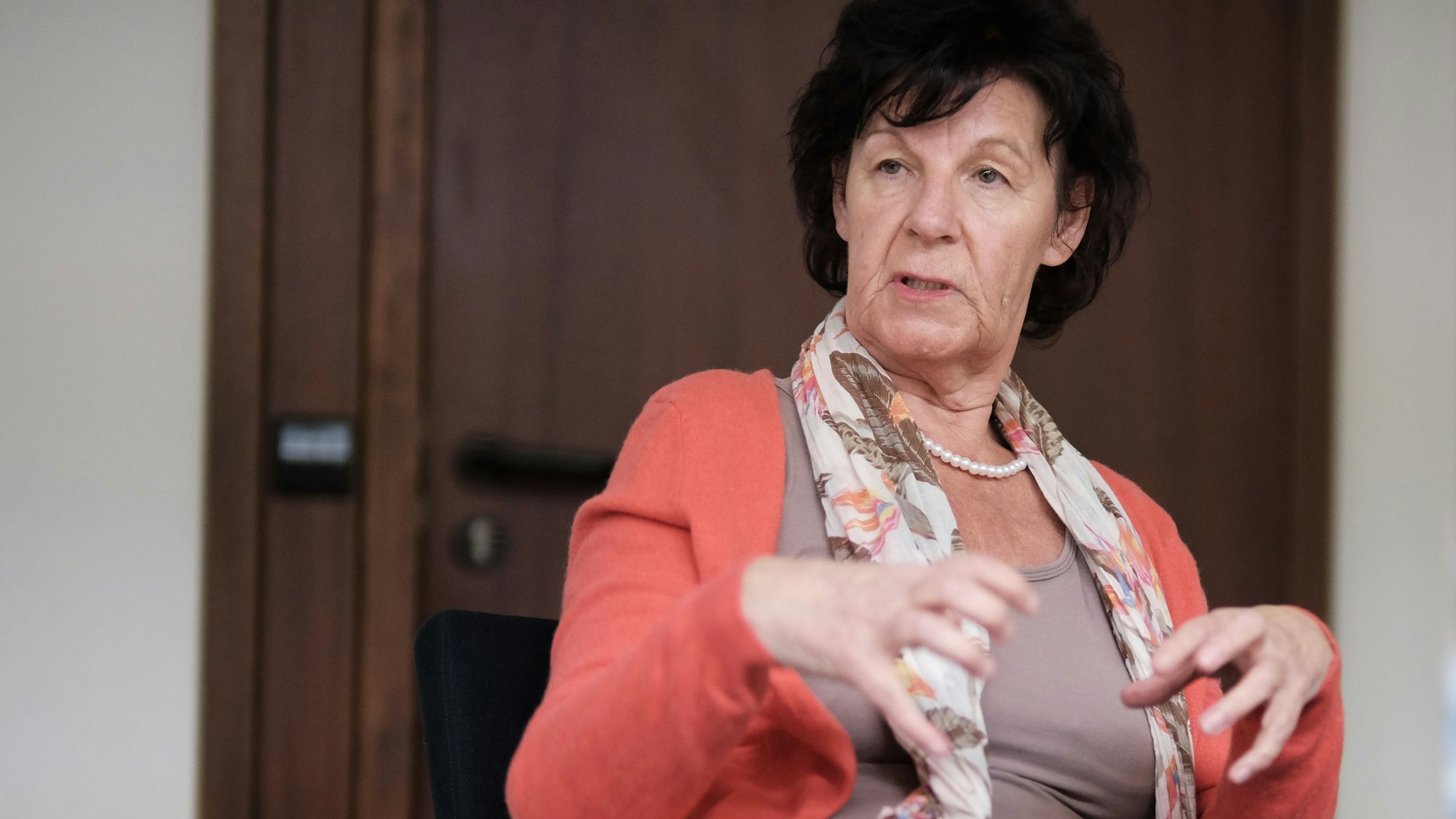 Eine Frau mit dunklem Haar sitzt gestikulierend an einem Tisch.