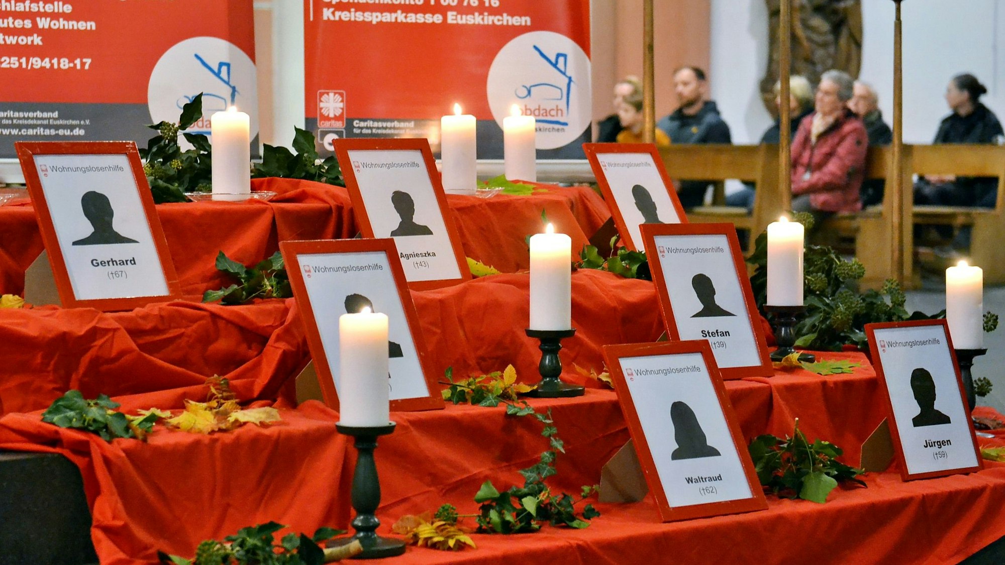 Auf einem roten Tuch, das auf den Treppen in der Kirche drapiert wurde, stehen Bilderrahmen mit den Namen der verstorbenen Wohnungslosen.