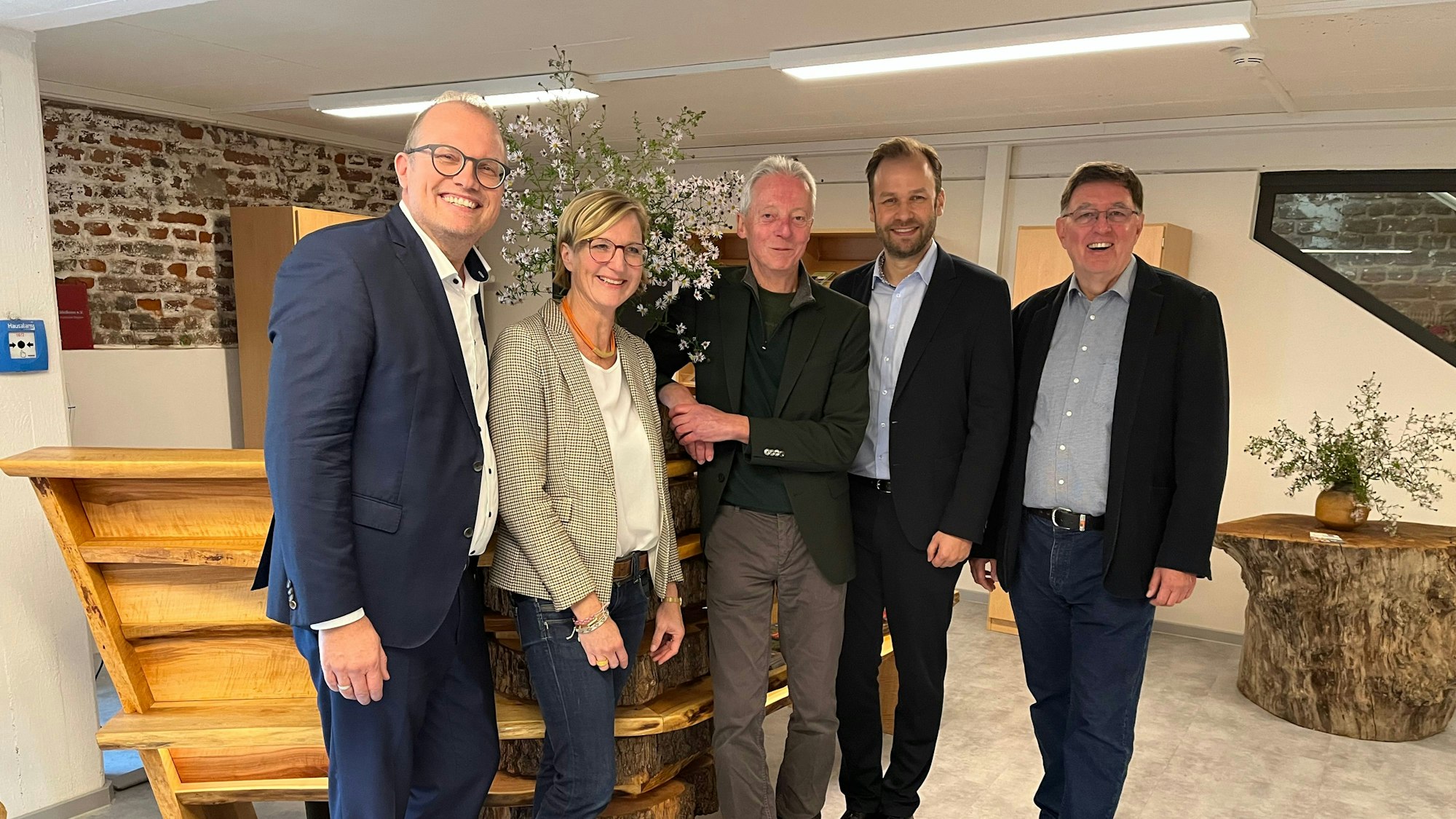 Vier Männer und eine Frau stehen nebeneinander in einer Eingangshalle mit Holzmöbeln.