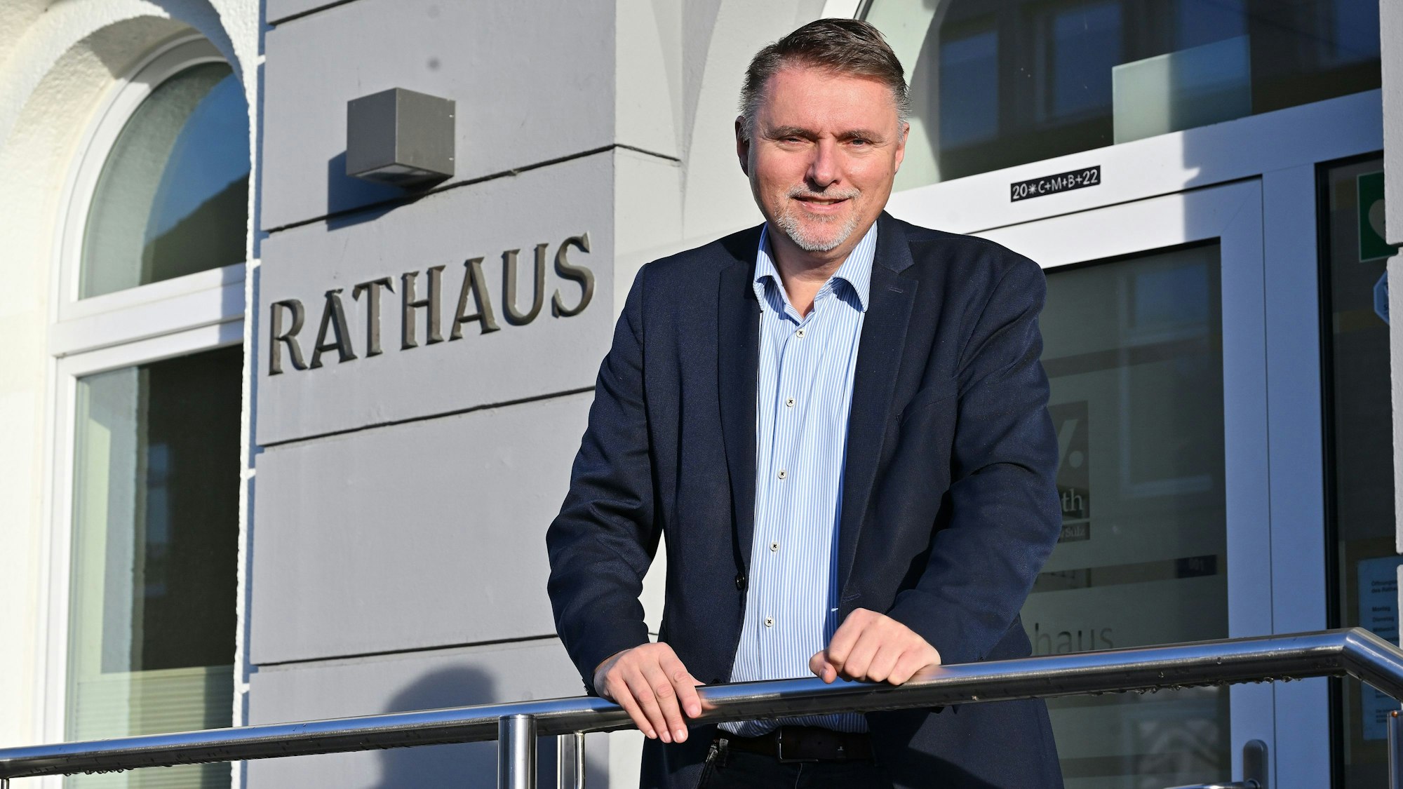 Ein Mann steht vor einem Gebäude mit der Aufschrift „Rathaus“.