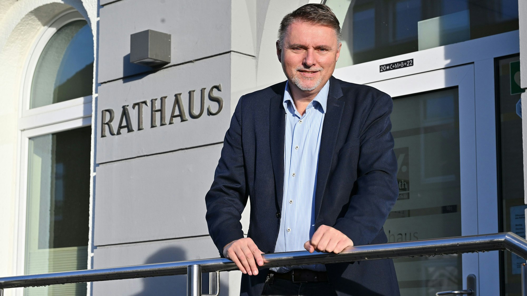 Ein Mann mittleren Alters steht an ein Geländer gelehnt vor einem Rathaus. Er heißt Michael Eyer und ist Bürgermeister von Overath.