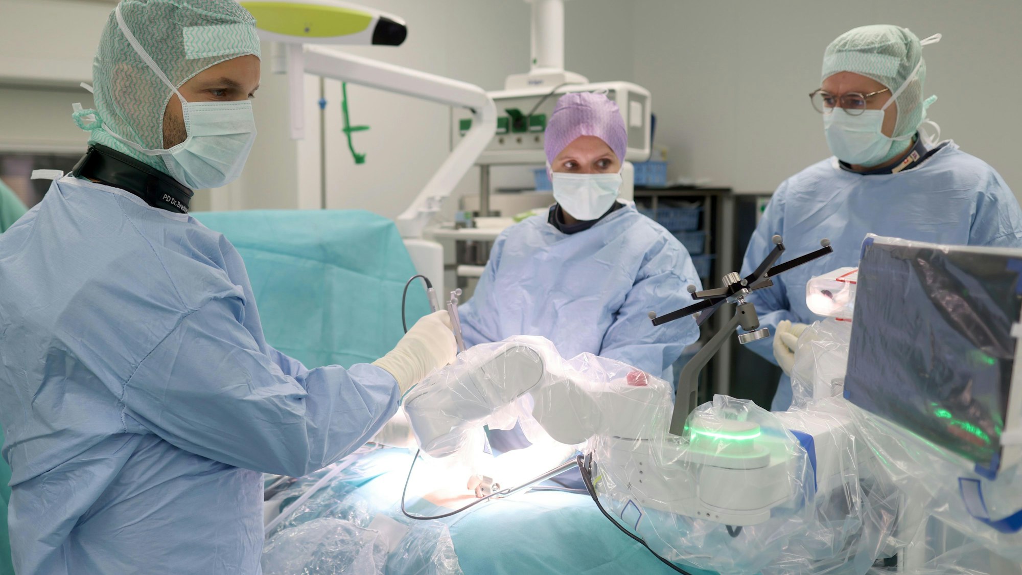 Prof. Dr. Jan Bredow (l.) und Dr. Franziska Wallscheid (Mitte) können auf einem Bildschirm von „Mazor“ ihren Eingriff in der Wirbelsäule des Patienten beobachten.