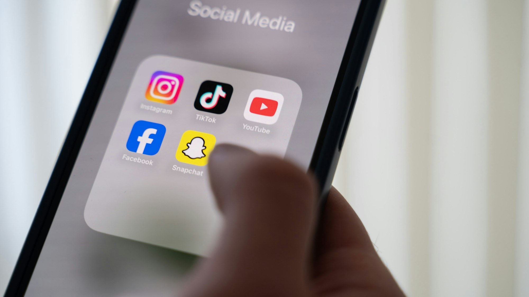 Eine Frau hält ein Smartphone, auf dessen Display verschiedene Social Media Apps angezeigt werden.