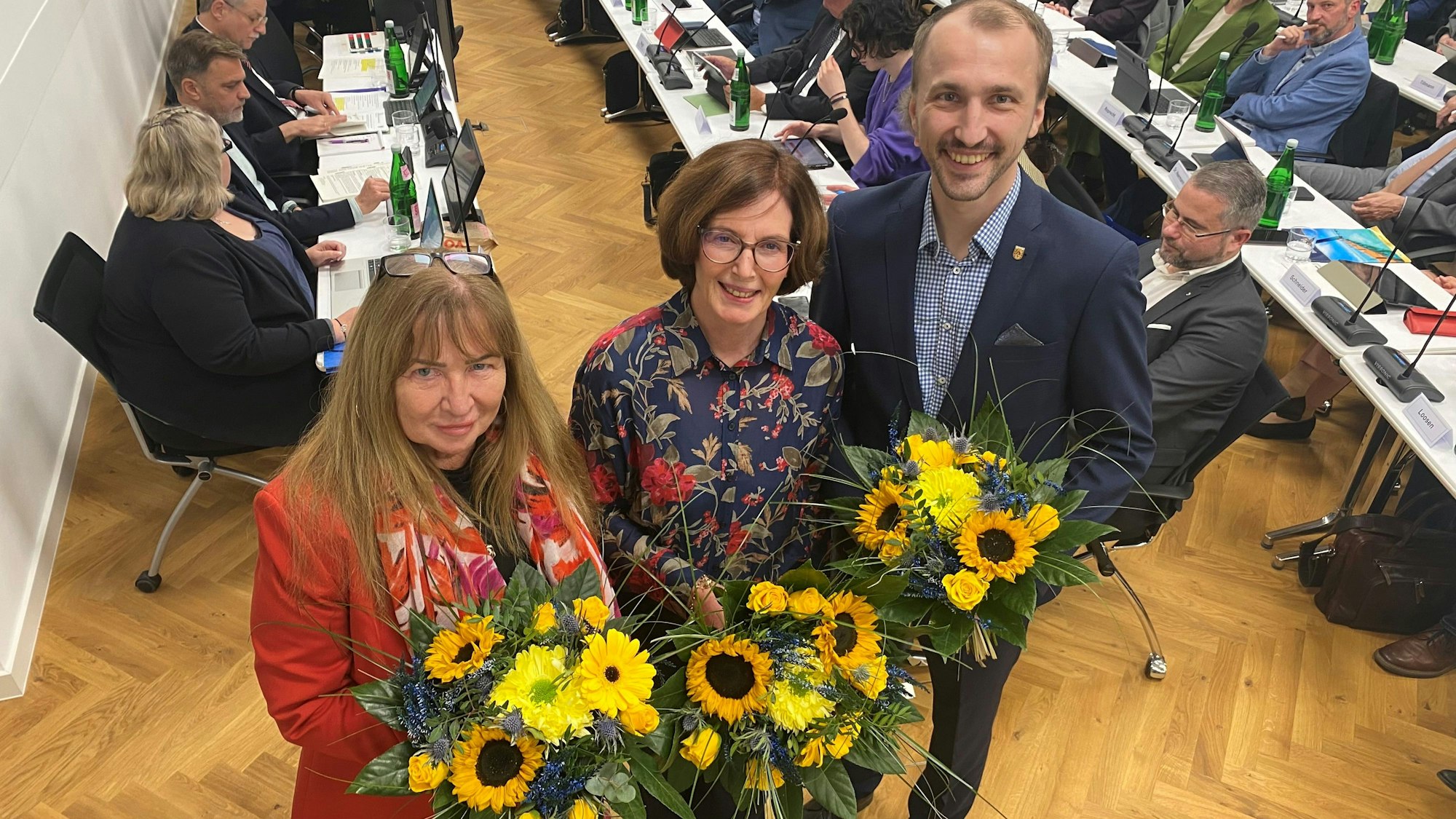 Zu sehen sind Hildegard Venghaus, Pia Regh und Robert Saß, die Blumensträuße in ihren Händen halten.