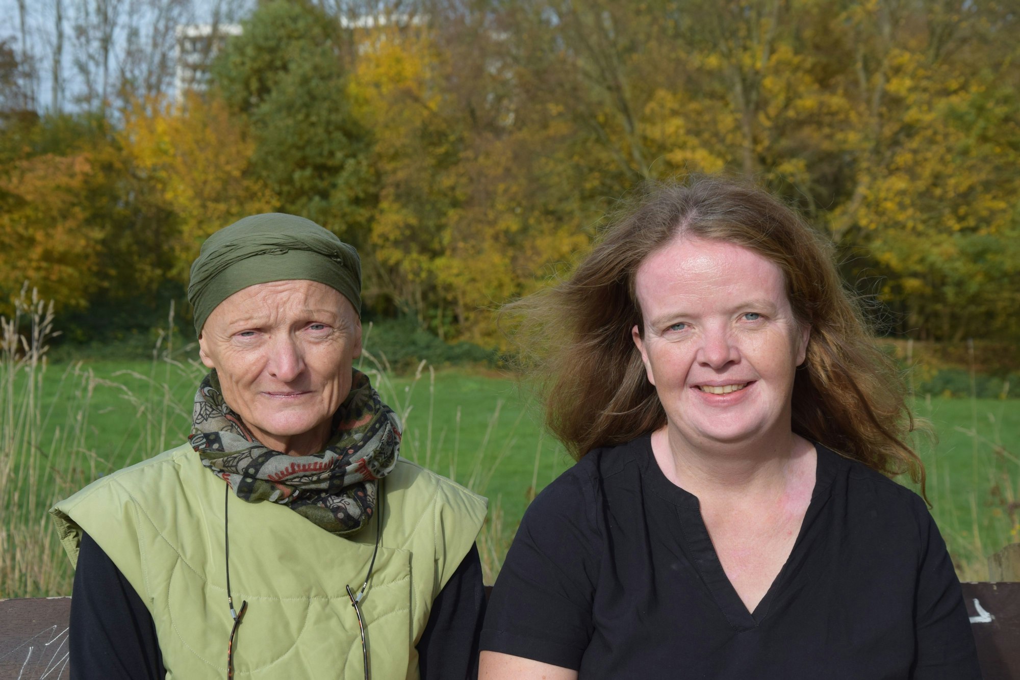 Eine Frau mit grünem Hut und eine jüngere Frau mit langem braunem Haar sitzen nebeneinander auf einer Bank.
