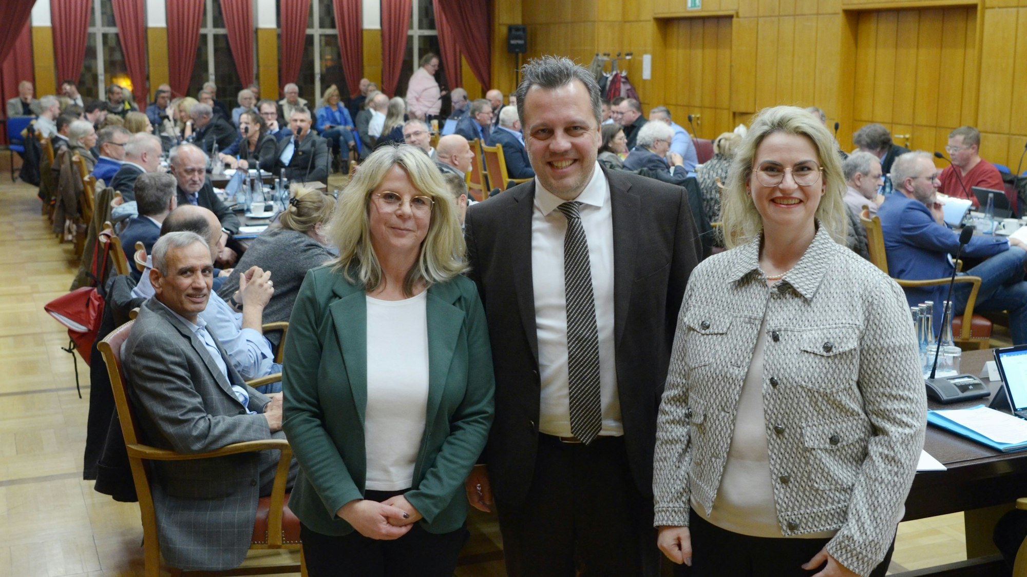 Das Bild zeigt den Bürgermeister und seine Stellvertreterinnen im Ratssaal, im Hintergrund weitere Stadtverordnete.