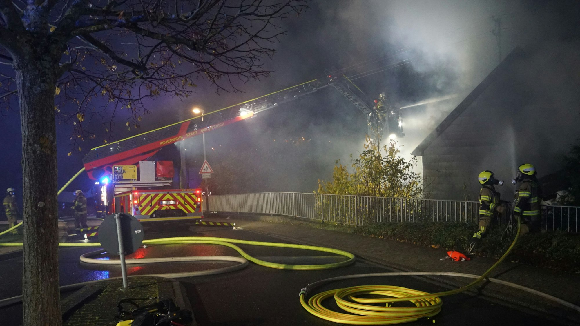 Die Drehleiter der Feuerwehr Mechernich steht auf der Straße. Aus dem Korb wird ein brennendes Haus gelöscht.