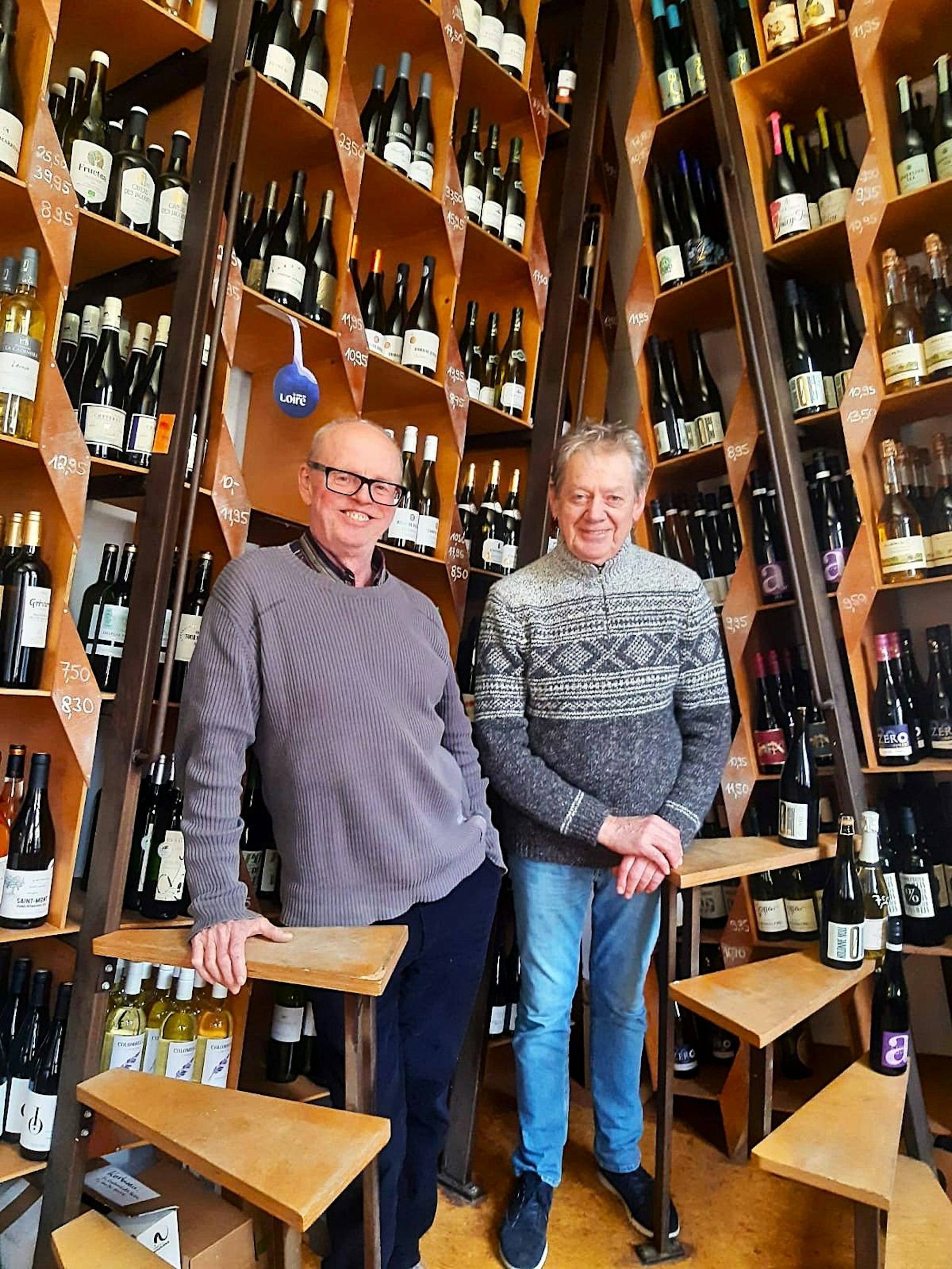 Zwei Männer stehen nebeneinander vor Weinregalen.