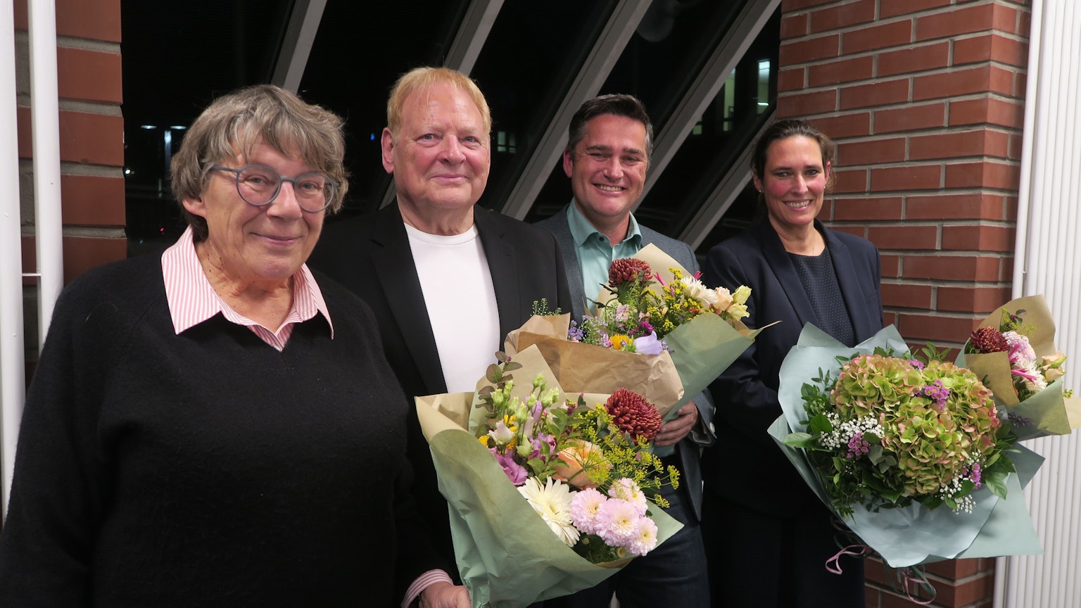 Zwei Frauen und zwei Männer stehen mit Blumensträußen in der Hand nebeneinander.