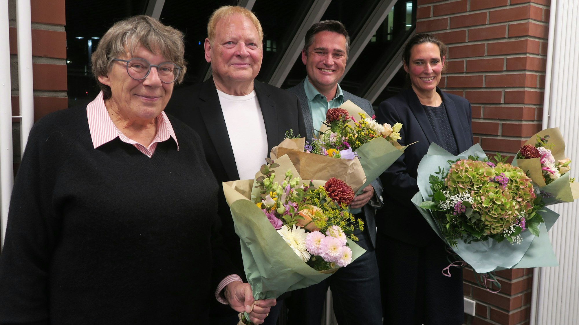 Zwei Frauen und zwei Männer stehen mit Blumensträußen in der Hand nebeneinander.