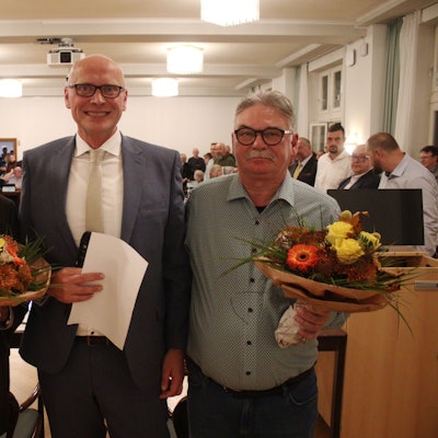Rechts und links vom Bürgermeister stehen dessen Stellvertreter, die beide Blumen in den Händen halten.