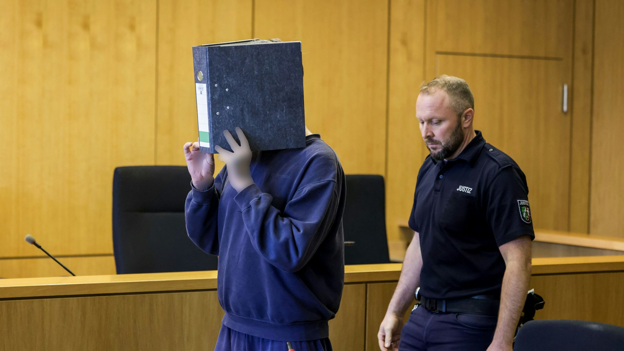 Aachen: Der angeklagte Krankenpfleger (l.) kommt am Mittwoch (5. November) mit einem Aktenordner vor dem Gesicht in den Gerichtssaal.