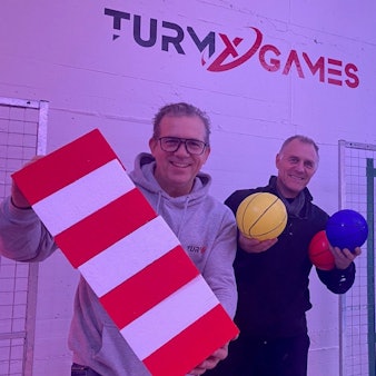 Zu sehen sind Achim Heymann, Marco Gleißner und Raimund Bechtloff, sie halten Gameshow-Equipment in den Händen.