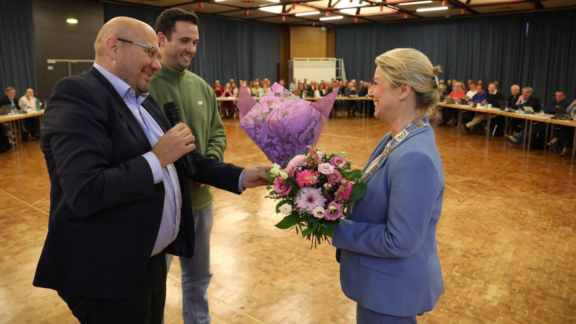 Zwei Männer überreichen einen Blumenstrauß an eine Frau.