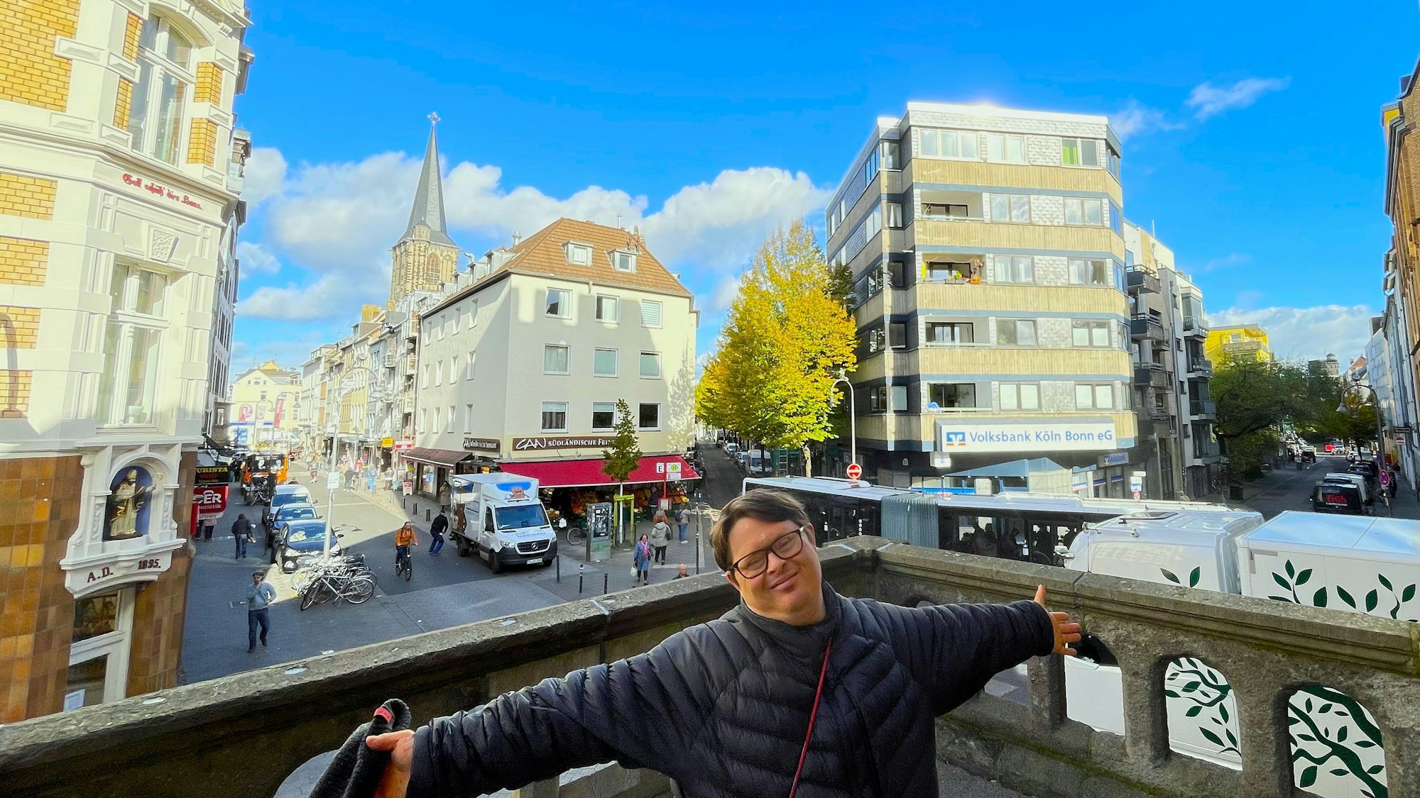 Ein junger Mann steht mit ausgebreiteten Armen, im Hintergrund ist die Severinstraße zu sehen.