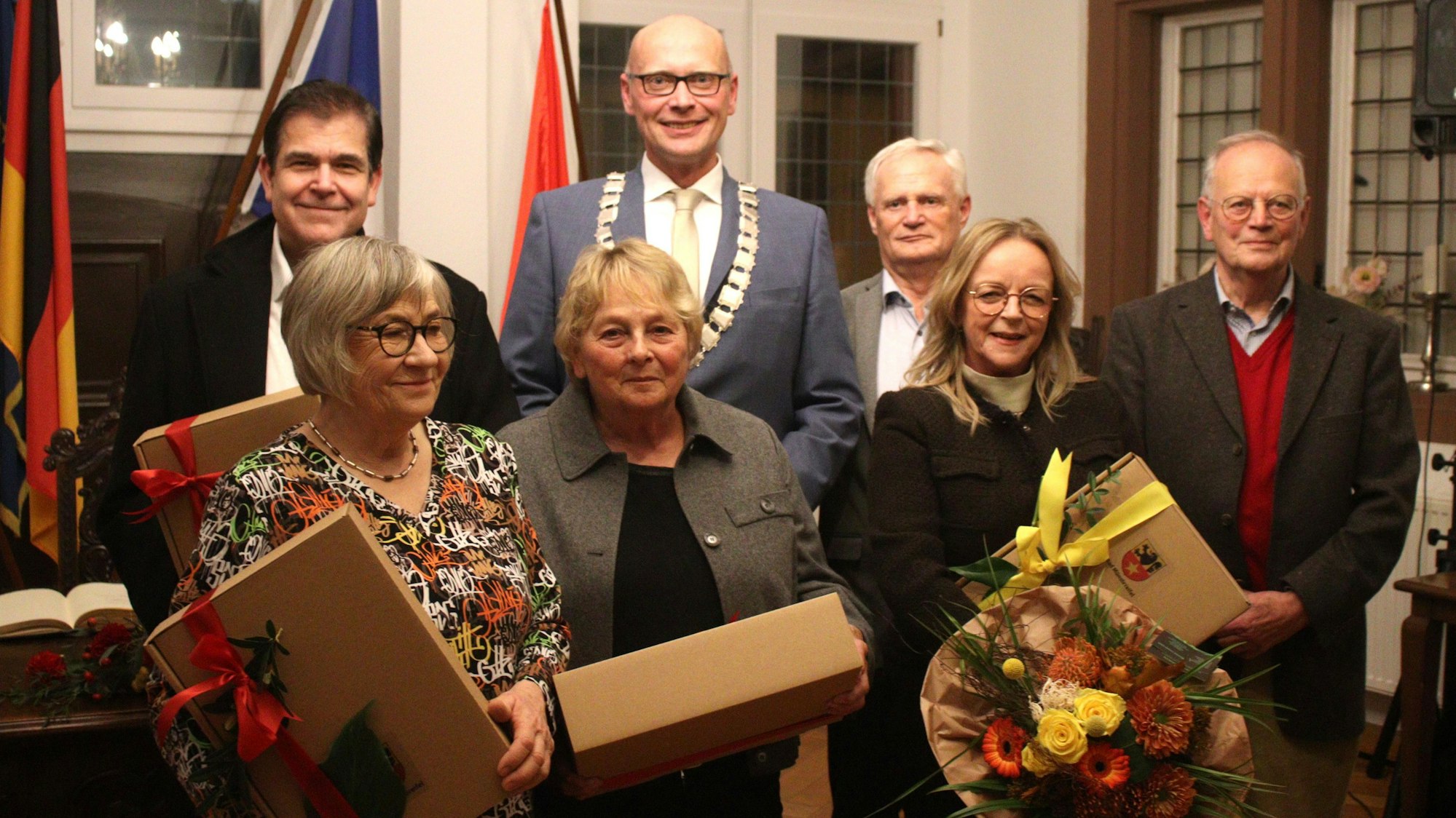 Drei Frauen mit Präsenten in der Hand stehen im Vordergrund, dahinter vier Männer.