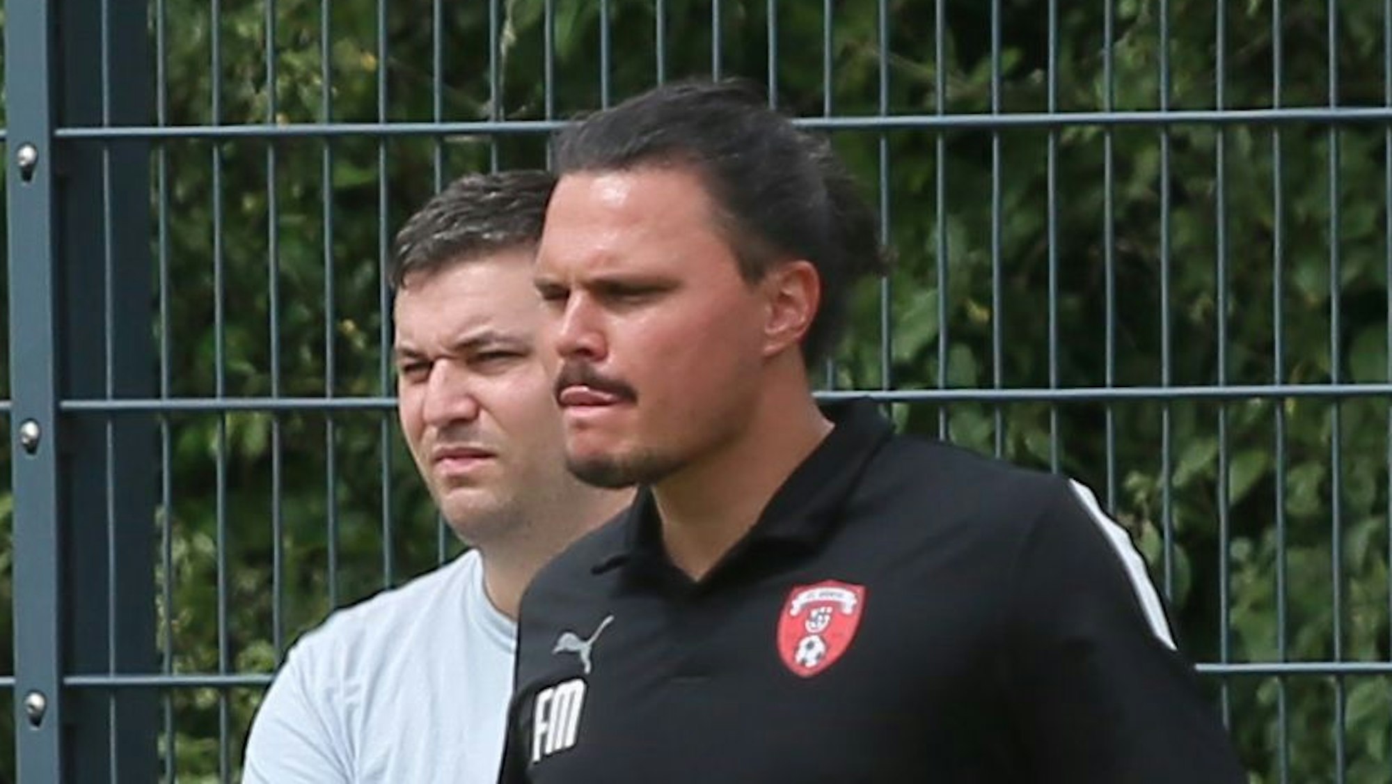 Das Bild zeigt Fabian Montabell in einem schwarzen T-Shirt, der das Spiel seiner Elf beobachtet.