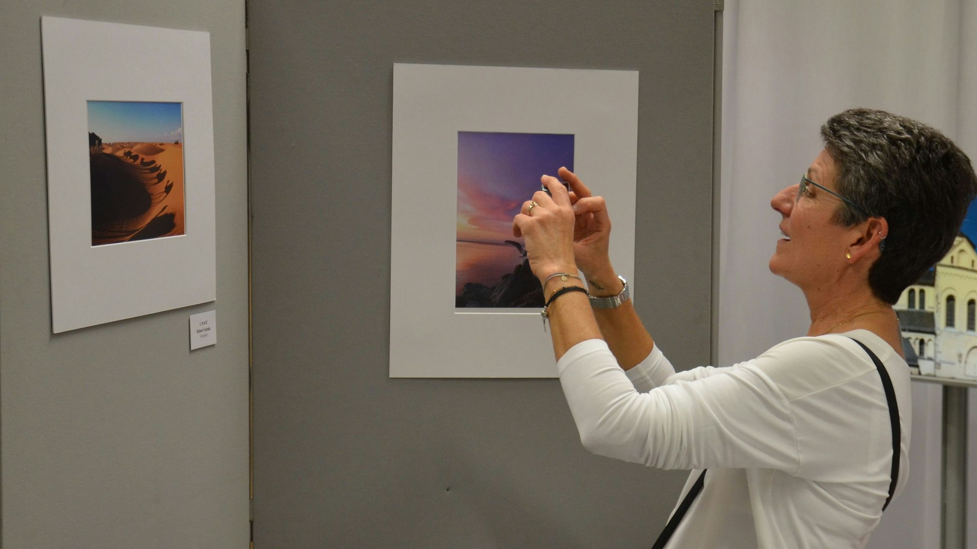 Zu sehen ist eine Frau, die eine Aufnahme von einem ausgestellten Foto macht.