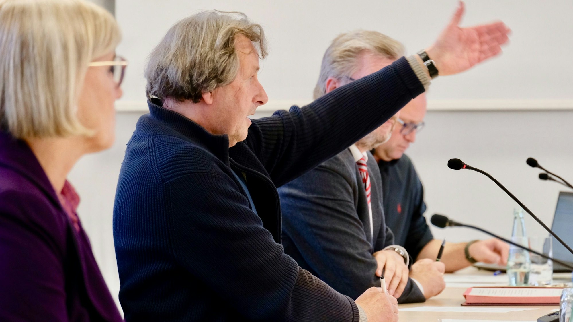 Ein Mann in dunklem Pullover sitzt an einem Tisch und gestikuliert.