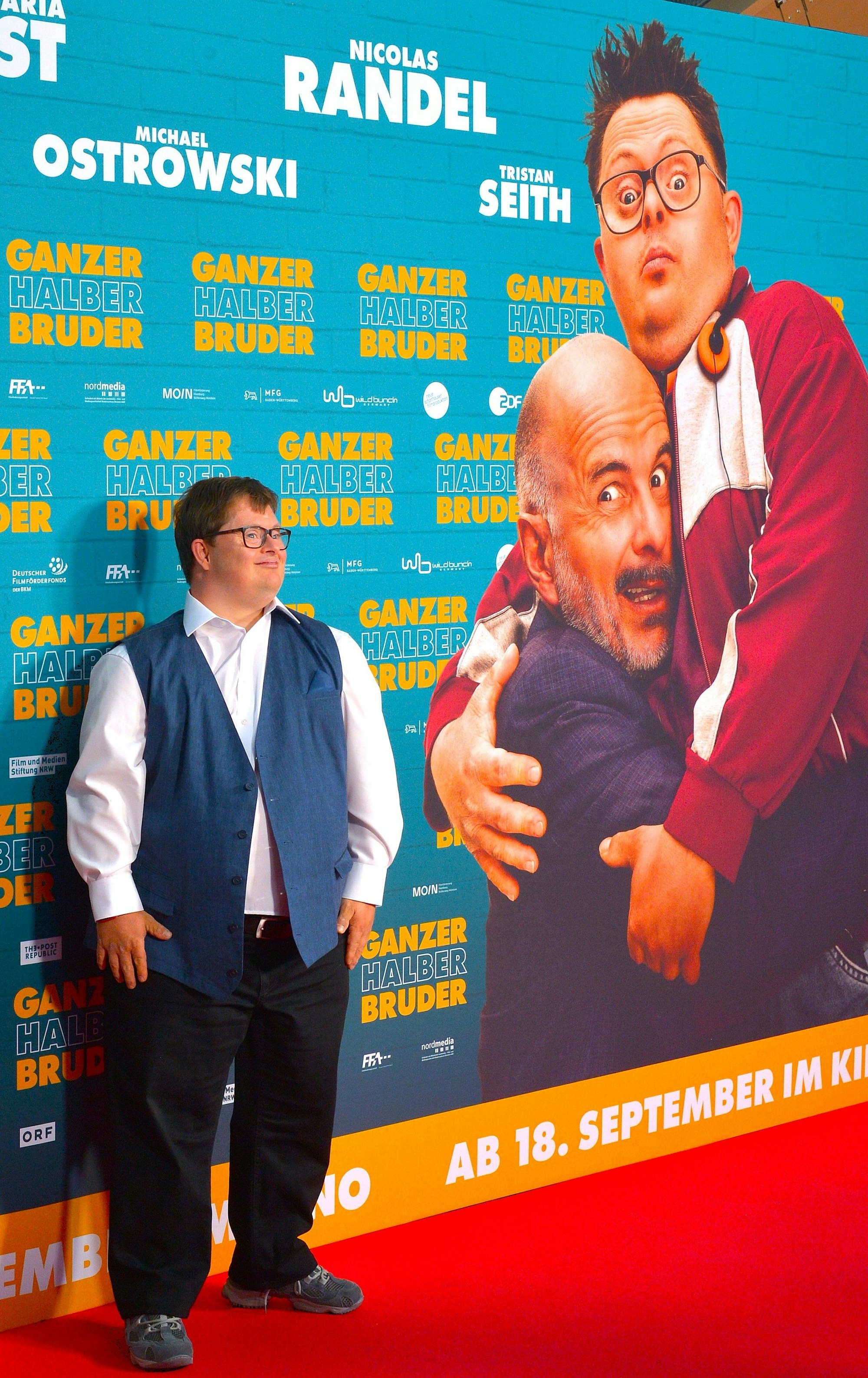 Ein junger Mann steht vor einem großen Filmplakat.