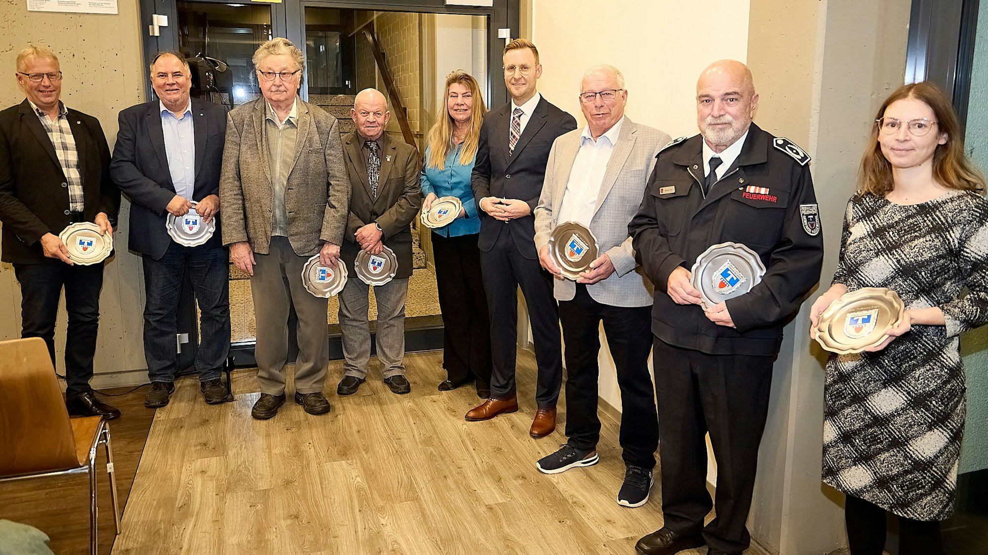 Ehemalige Ratsmitglieder der Gemeinde Hellenthal stehen in einer Reihe. Alle haben einen Wappenteller in der Hand, den sie geschenkt bekommen haben.