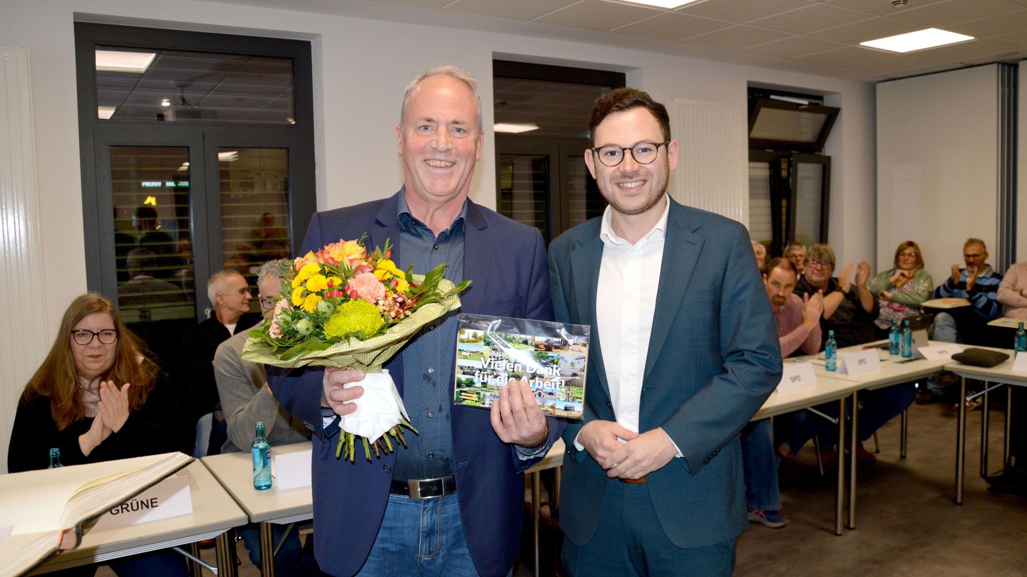 Hermann-Josef Esser (l.) hält einen Blumenstrauß und ein Präsent in den Händen, Emmanuel Kunz steht neben ihm.