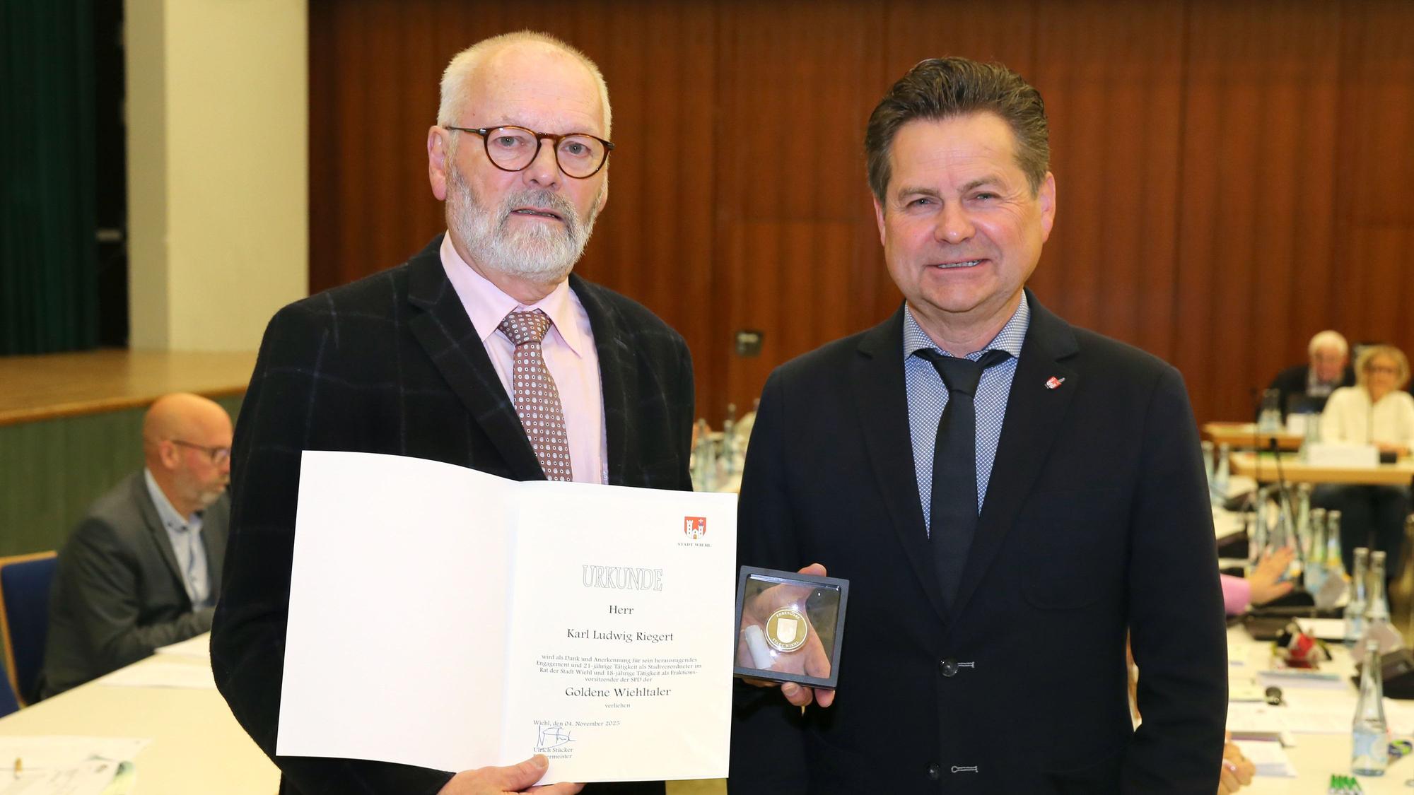 Zwei Männer, der linke hält eine Urkunde und eine Münze.