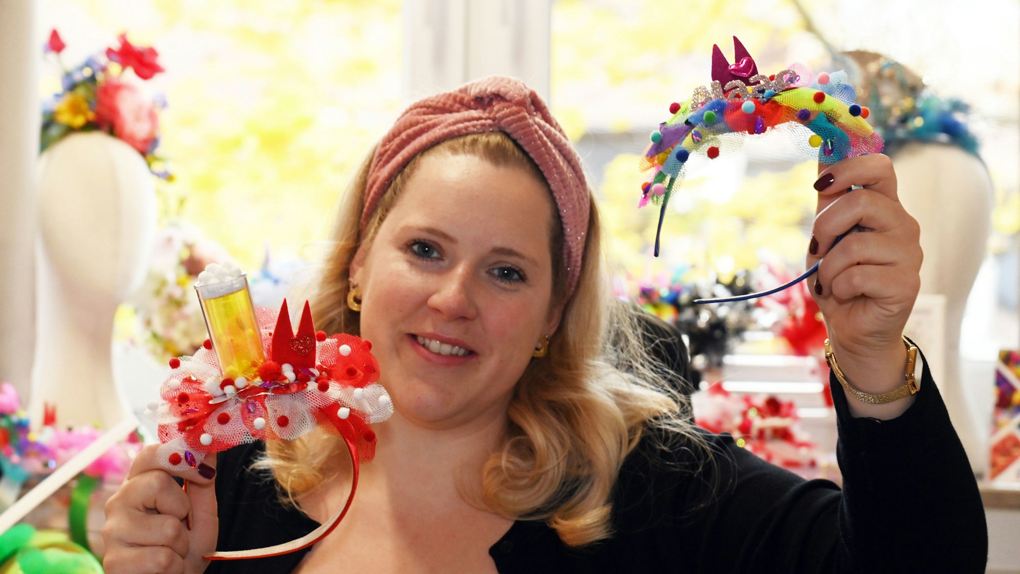 Ein Frau mit blondem Haar und Haarband hält zwei bunt dekorierte und gebastelte Haarreifen in den Händen.