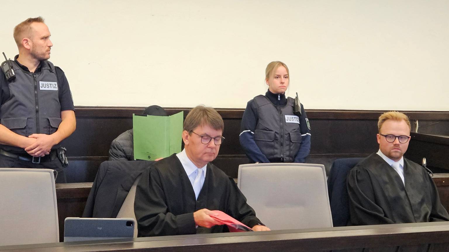 Mit einem Aktenordner versucht der Angeklagte sein Gesicht zu verbergen.