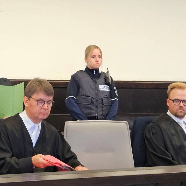 Mit einem Aktenordner versucht der Angeklagte sein Gesicht zu verbergen.