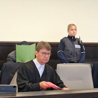 Mit einem Aktenordner versucht der Angeklagte sein Gesicht zu verbergen.