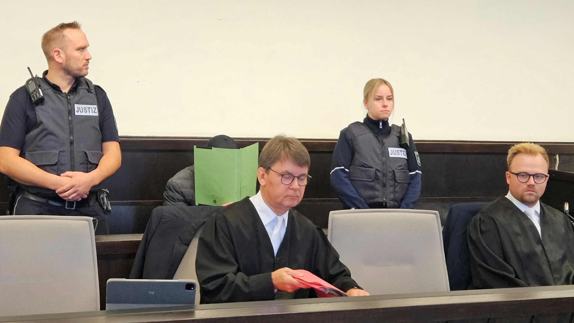 Mit einem Aktenordner versucht der Angeklagte sein Gesicht zu verbergen.