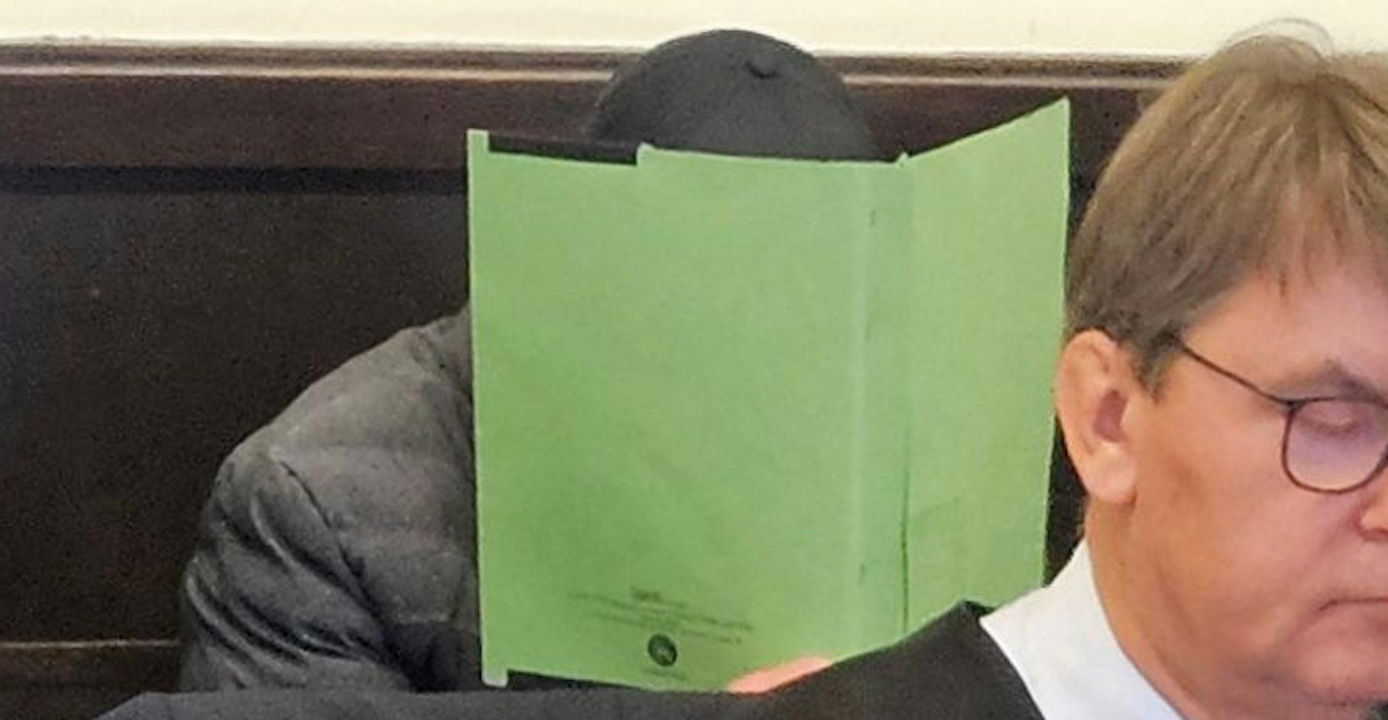 Ein Angeklagter sitzt mit einem Aktendeckel vor dem Gesicht auf der Anklagebank des Paderborner Landgerichts.