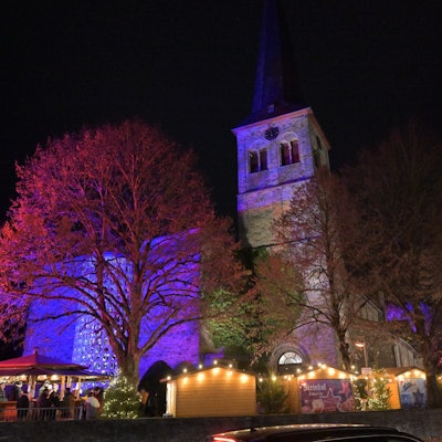 Der Overather Weihnachtsmarkt und die angestrahlte Kirche St. Walburga am Abend.