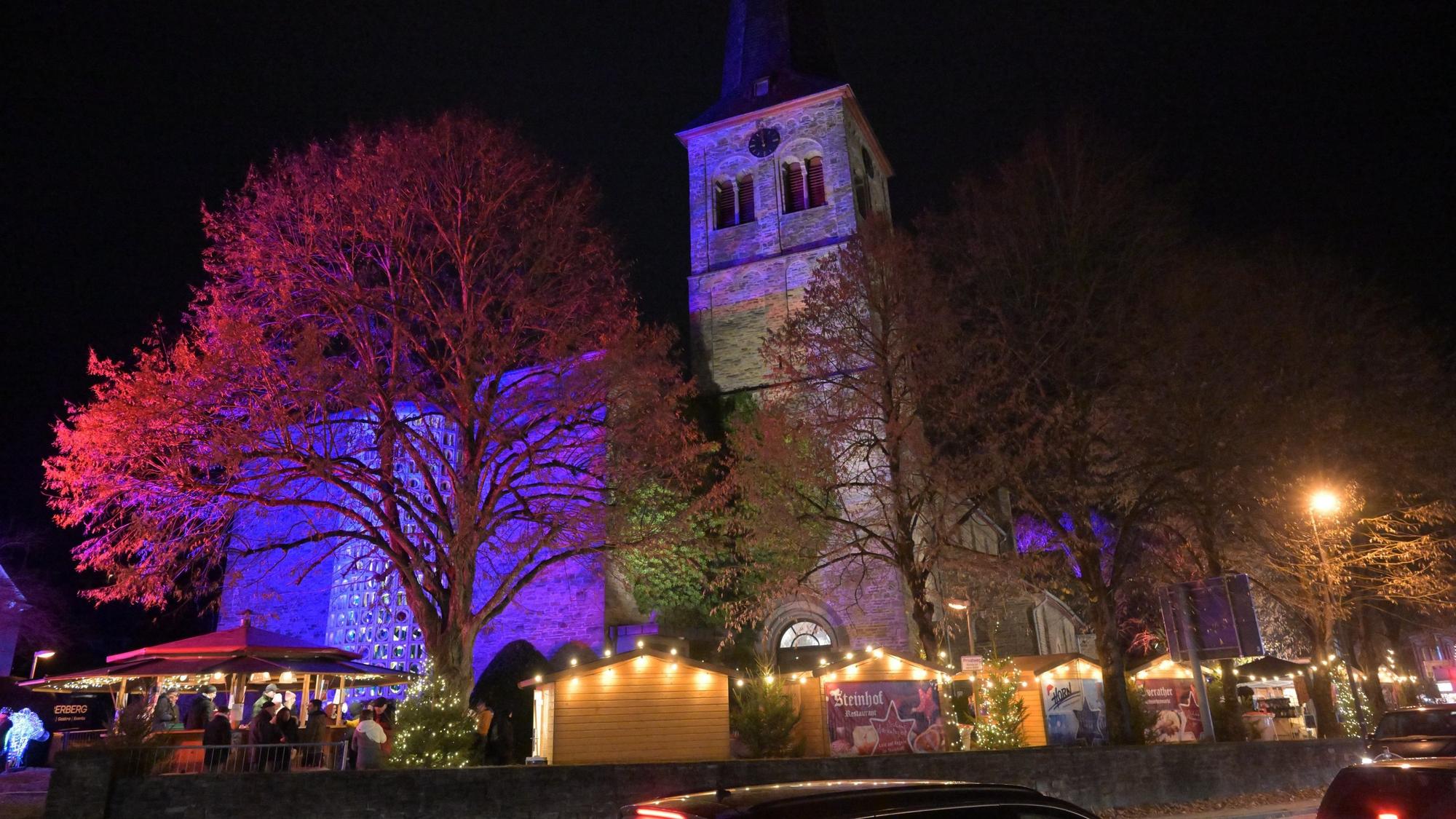 Der Overather Weihnachtsmarkt und die angestrahlte Kirche St. Walburga am Abend.